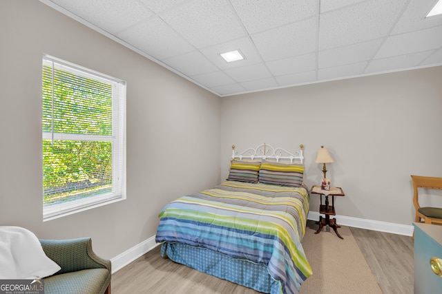 bedroom with a paneled ceiling, baseboards, and wood finished floors