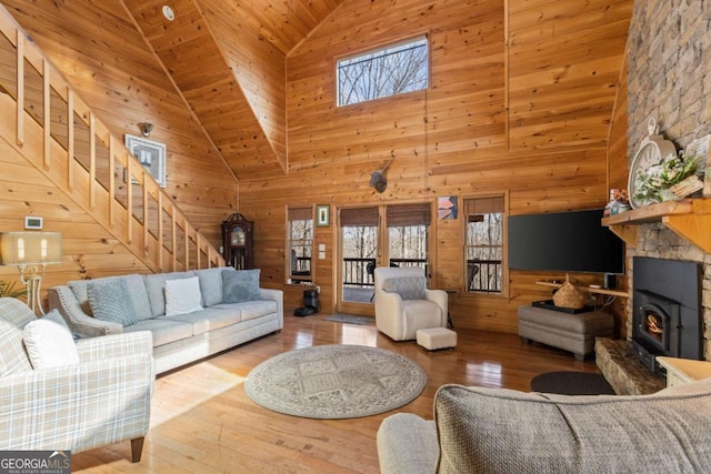 living room featuring stairway, wood-type flooring, wooden walls, and a wood stove