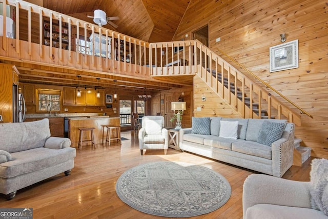 living room with light wood-type flooring, a ceiling fan, wood walls, and wooden ceiling