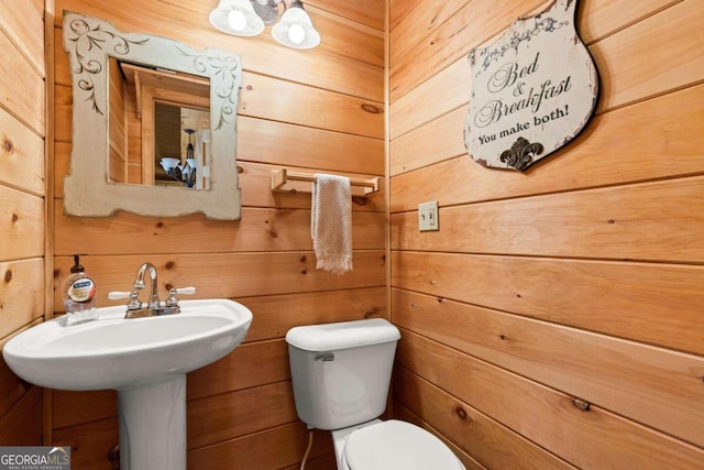 bathroom featuring a sink, toilet, and wood walls