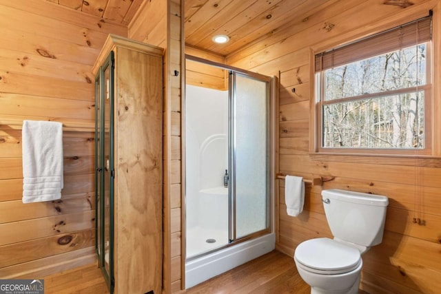 bathroom featuring toilet, wood finished floors, a stall shower, and wood walls