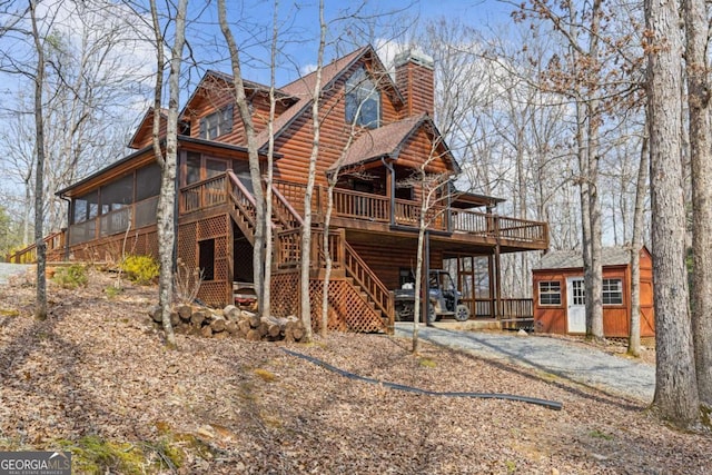 view of front facade with a chimney, a deck, faux log siding, a sunroom, and stairs