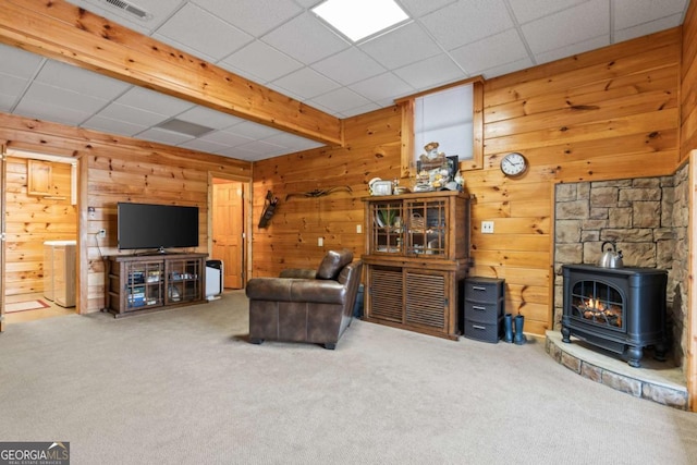 living room featuring visible vents, carpet floors, wood walls, and a wood stove