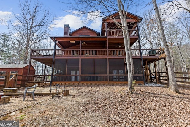 back of property featuring a chimney, a deck, a sunroom, an outbuilding, and log veneer siding