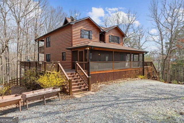 view of front of home featuring log veneer siding, stairway, and a sunroom