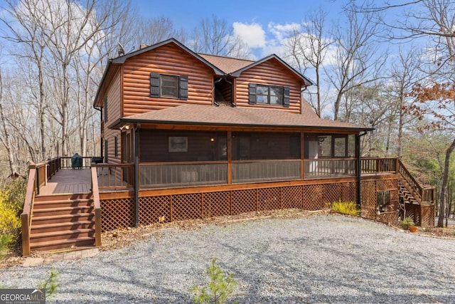 view of front of property featuring faux log siding, a shingled roof, stairway, a deck, and a sunroom