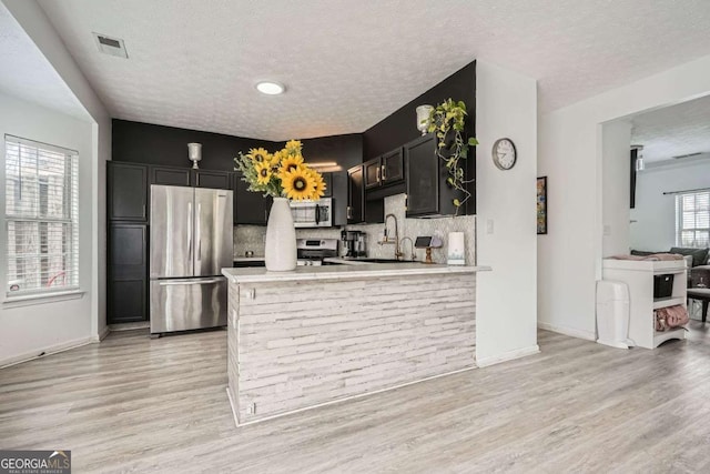 kitchen featuring dark cabinetry, light countertops, light wood-style floors, appliances with stainless steel finishes, and backsplash