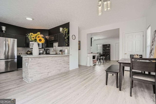 kitchen with decorative backsplash, light countertops, light wood-style floors, and freestanding refrigerator