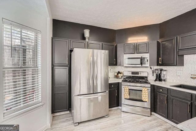 kitchen with stainless steel appliances, light wood-style flooring, decorative backsplash, and light countertops