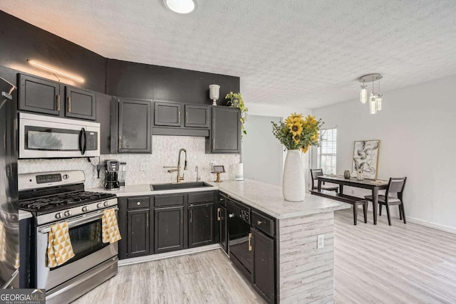 kitchen with light wood finished floors, backsplash, a peninsula, stainless steel appliances, and a sink