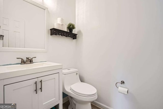half bathroom featuring toilet, vanity, and baseboards