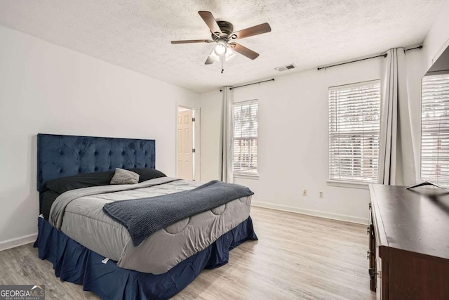 bedroom with light wood-type flooring, visible vents, a ceiling fan, a textured ceiling, and baseboards