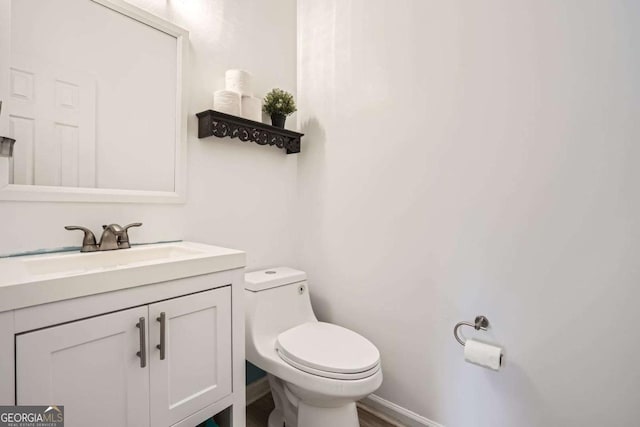 half bathroom with baseboards, toilet, and vanity