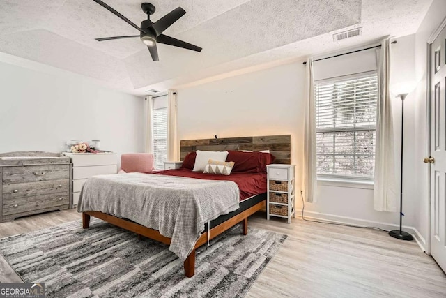 bedroom featuring wood finished floors, baseboards, visible vents, a tray ceiling, and a textured ceiling