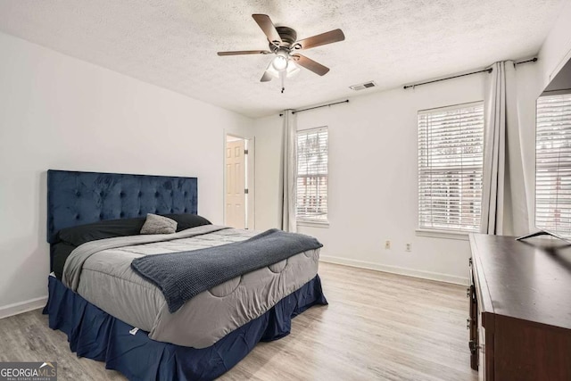 bedroom with visible vents, light wood-style flooring, a textured ceiling, baseboards, and ceiling fan