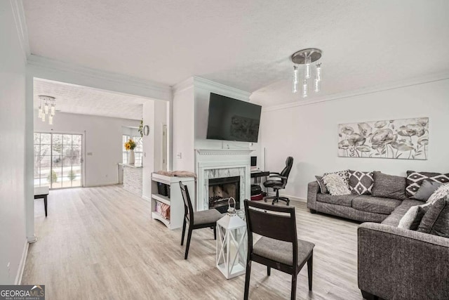 living area with light wood-style flooring, an inviting chandelier, ornamental molding, and a fireplace