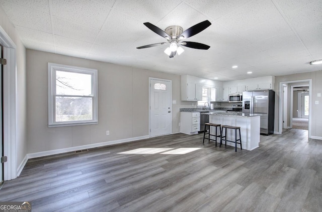 kitchen featuring a kitchen island, baseboards, appliances with stainless steel finishes, wood finished floors, and white cabinets