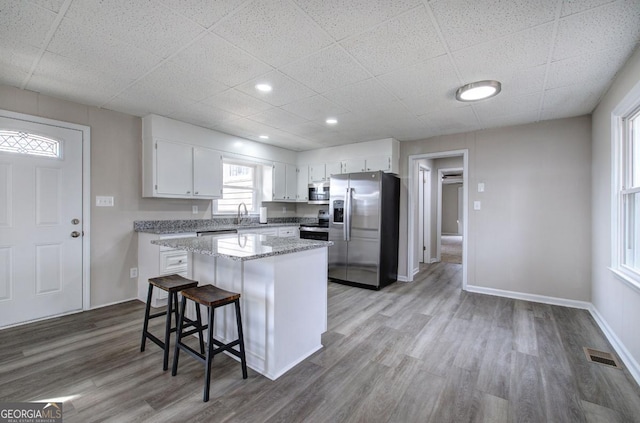 kitchen with a kitchen island, wood finished floors, white cabinets, stainless steel appliances, and a sink