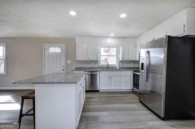 kitchen with light wood-type flooring, a breakfast bar, light stone counters, white cabinetry, and stainless steel appliances