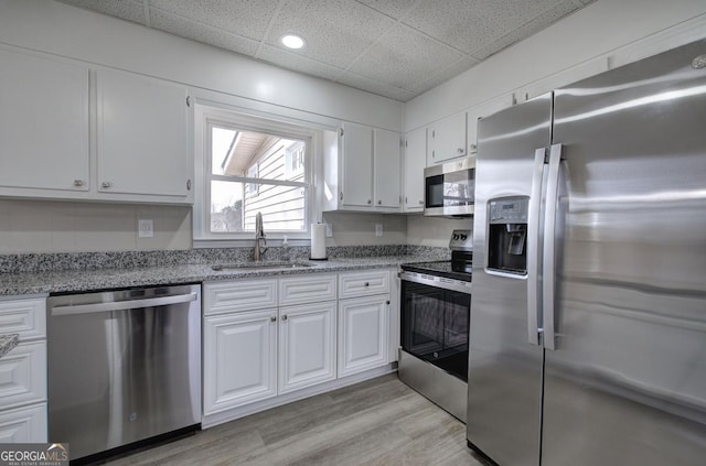 kitchen featuring a drop ceiling, stainless steel appliances, light wood-style floors, white cabinetry, and a sink