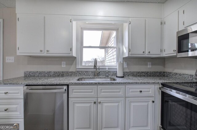 kitchen featuring light stone counters, white cabinetry, stainless steel appliances, and a sink