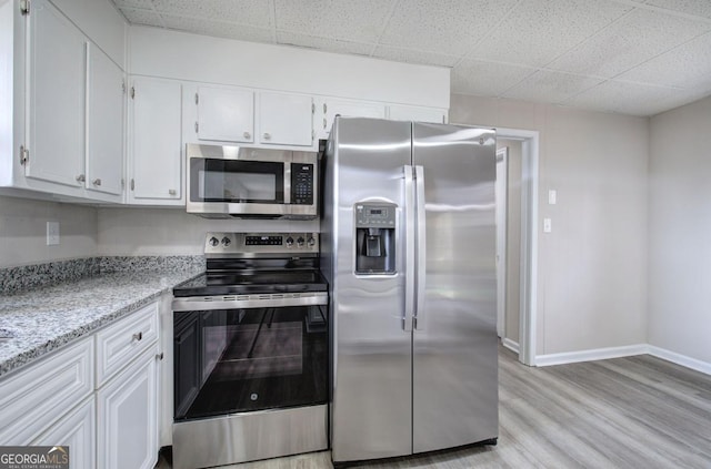 kitchen with light stone countertops, baseboards, appliances with stainless steel finishes, white cabinetry, and light wood-type flooring