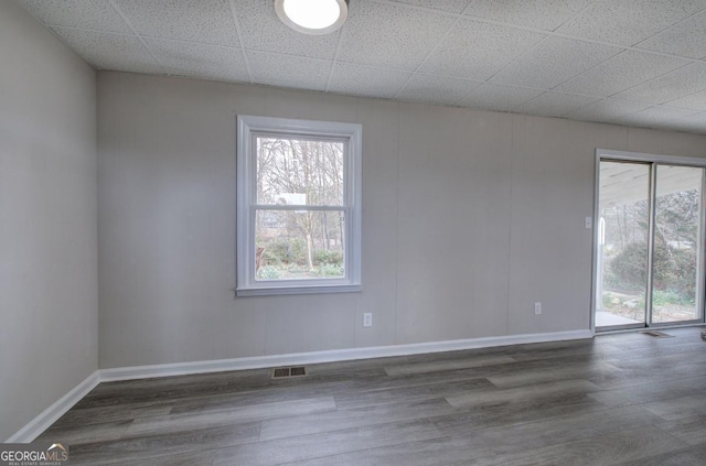 empty room featuring baseboards, wood finished floors, visible vents, and a paneled ceiling