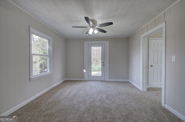 empty room featuring a healthy amount of sunlight, crown molding, ceiling fan, and carpet floors