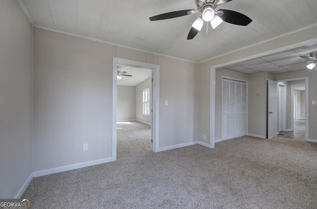 carpeted spare room with baseboards, crown molding, and a ceiling fan