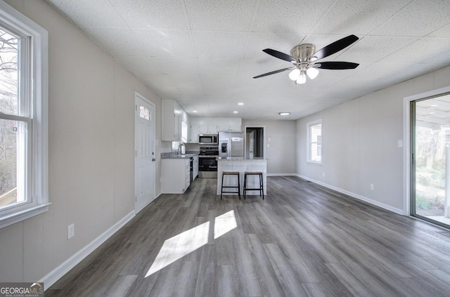 unfurnished living room with ceiling fan, baseboards, dark wood finished floors, and a sink