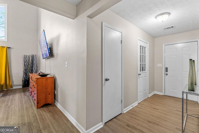 foyer entrance with baseboards, wood finished floors, visible vents, and a textured ceiling