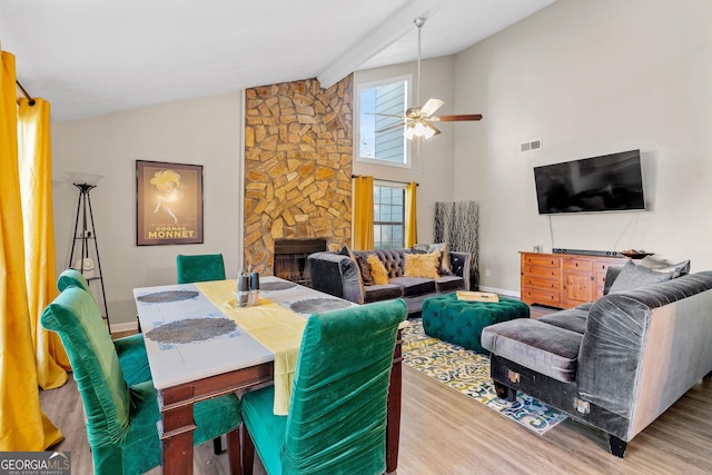 dining space with visible vents, a ceiling fan, wood finished floors, a stone fireplace, and baseboards