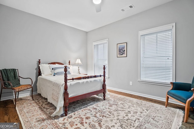 bedroom with multiple windows, wood finished floors, visible vents, and baseboards