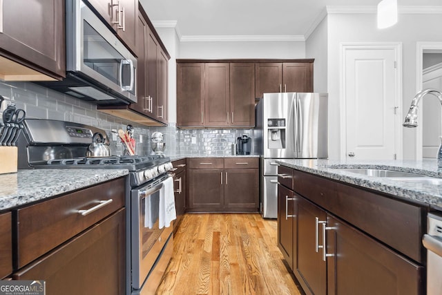 kitchen with light wood-style flooring, a sink, ornamental molding, stainless steel appliances, and dark brown cabinets