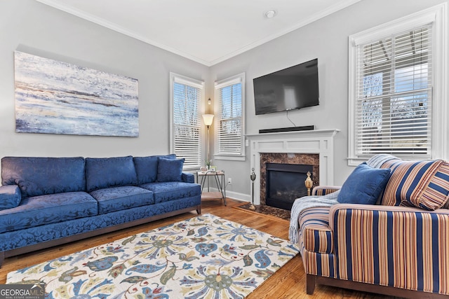 living area featuring a fireplace, crown molding, baseboards, and wood finished floors