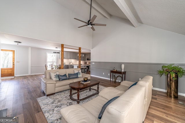 living area featuring beam ceiling, high vaulted ceiling, a ceiling fan, wood finished floors, and baseboards