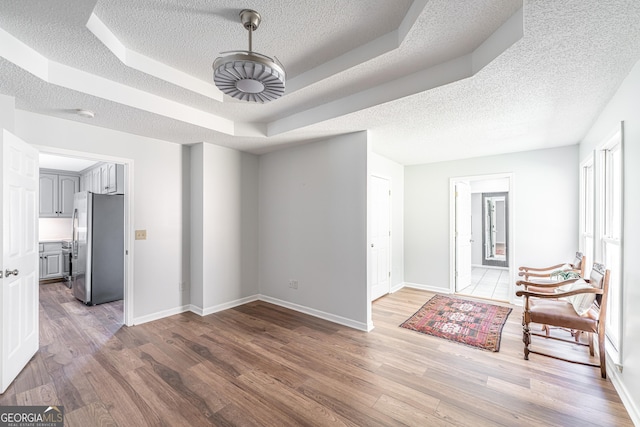 interior space featuring a textured ceiling, baseboards, a tray ceiling, and wood finished floors