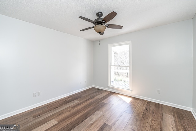 empty room featuring baseboards, a textured ceiling, dark wood-style floors, and a ceiling fan