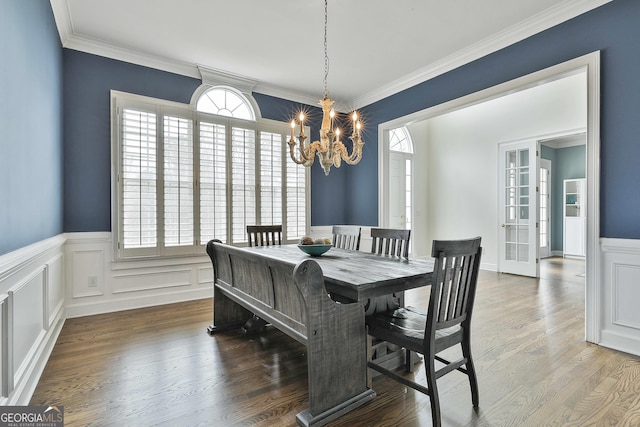 dining area with a decorative wall, ornamental molding, wood finished floors, and a chandelier