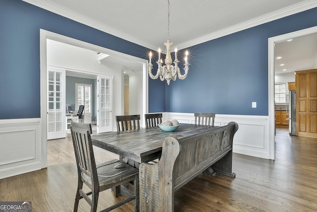 dining area featuring dark wood finished floors, wainscoting, an inviting chandelier, and ornamental molding