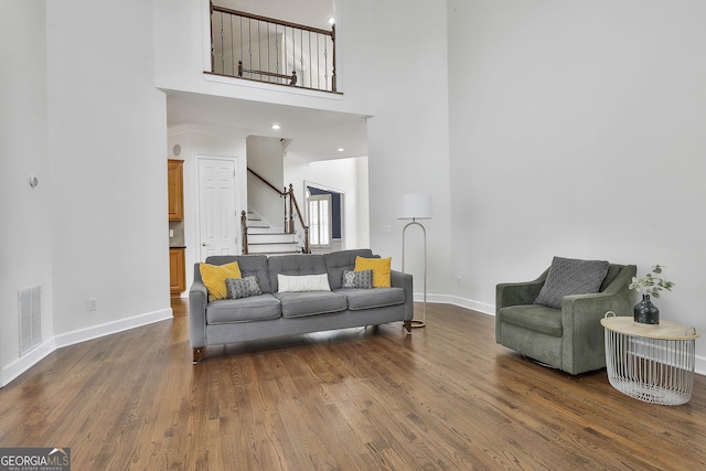 living room with stairway, wood finished floors, visible vents, baseboards, and a high ceiling