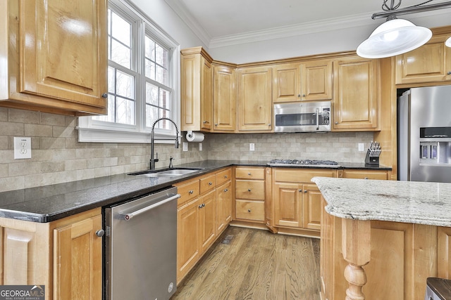 kitchen featuring dark stone countertops, a sink, stainless steel appliances, light wood-style floors, and crown molding