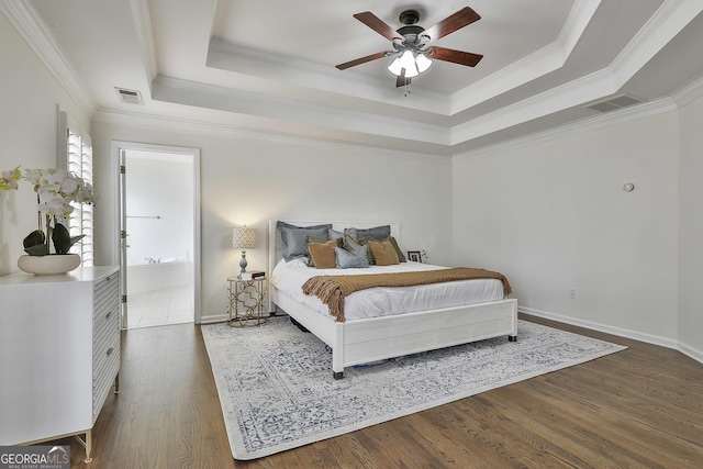 bedroom featuring visible vents, ornamental molding, a tray ceiling, wood finished floors, and baseboards