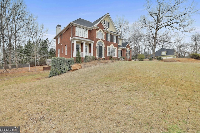 georgian-style home featuring brick siding, a chimney, a front lawn, and fence