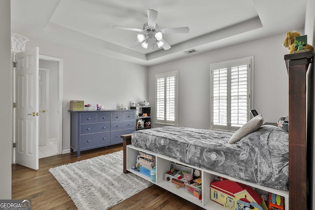 bedroom featuring a ceiling fan, a tray ceiling, wood finished floors, and visible vents