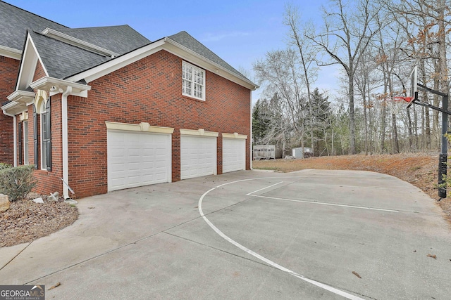 view of side of home with an attached garage, brick siding, driveway, and roof with shingles