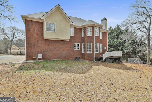 view of side of property with a wooden deck, central air condition unit, brick siding, and a chimney