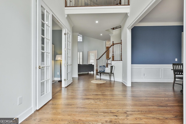 entryway featuring wood finished floors, a wainscoted wall, french doors, crown molding, and a decorative wall