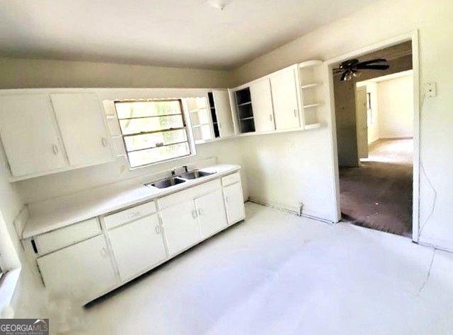 kitchen with a ceiling fan, concrete floors, open shelves, a sink, and white cabinetry