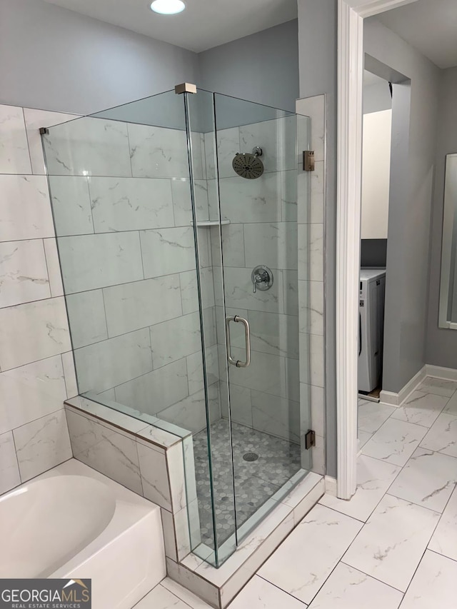 bathroom featuring baseboards, washer / dryer, a stall shower, a bath, and marble finish floor